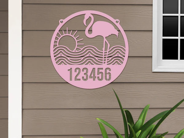 Pink-colored Flamingo Address Sign with house number '123456', waves, and sun design, mounted on door with beige wall.