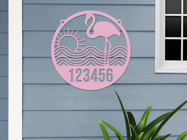 Pink-colored Flamingo Address Sign with house number '123456', waves, and sun design, mounted on door with gray-blue wall.