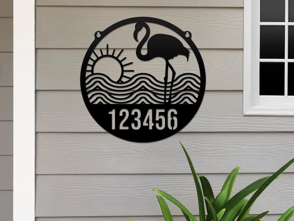 Black-colored Flamingo Address Sign with house number '123456', waves, and sun design, mounted on door with biege wall.