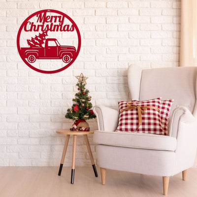 Decorative wall sign with Merry Christmas text and truck carrying tree, displayed above small Christmas tree and chair, festive holiday décor for seasonal home display