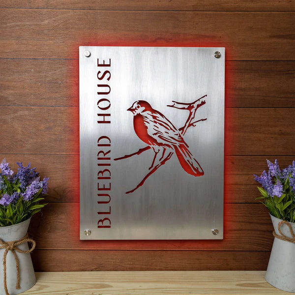 Aluminum sign laser cut and engraved, red backlit, mounted on wood, with vertical “BLUEBIRD HOUSE” and bird on branch design.