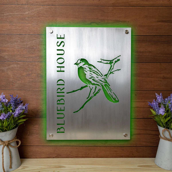 Aluminum sign laser cut and engraved, green backlit, mounted on wood, with vertical “BLUEBIRD HOUSE” and bird on branch design.