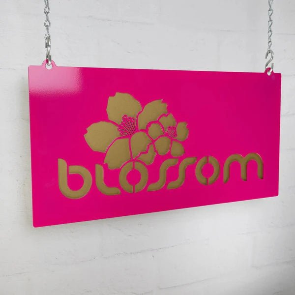 Pink decorative sign with gold floral design and text “Blossom” on white background, custom indoor or outdoor home décor accent