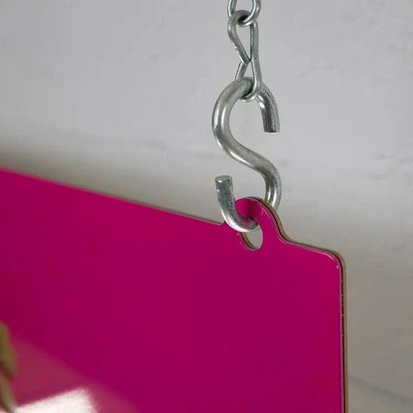 Metal hook attached to pink object on neutral background, showcasing hardware detail for home décor or functional accessory