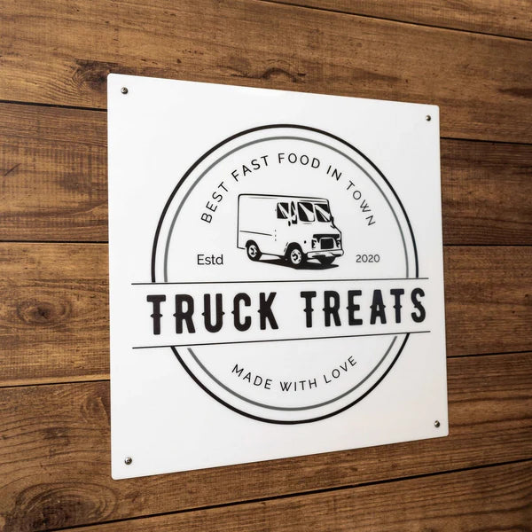 Rectangular sign on wood with circular design, food truck graphic, “TRUCK TREATS” text, and “BEST FAST FOOD IN TOWN” slogan.