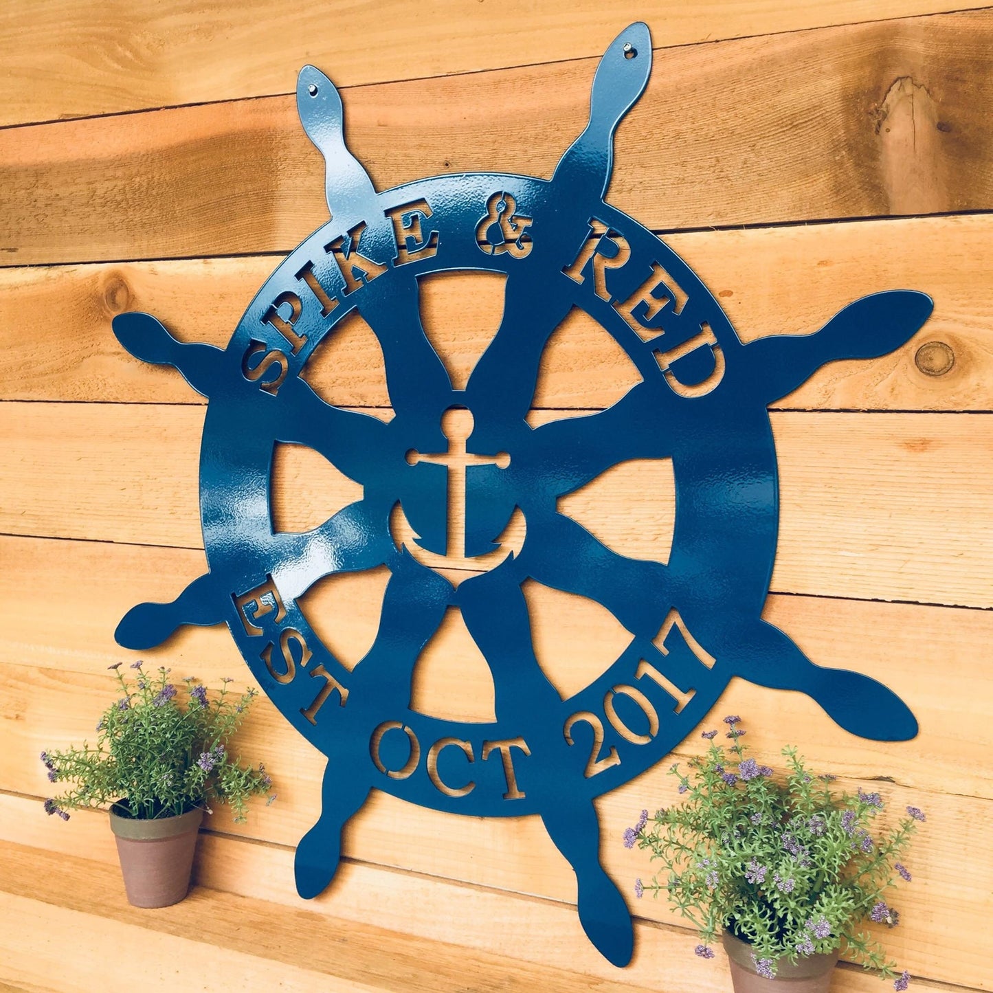 Nautical Captain's Ship Wheel Metal Door Hanger displayed on a wooden wall, showcasing its intricate cut-out design, ideal for personalized beach house decor or boater gifts.