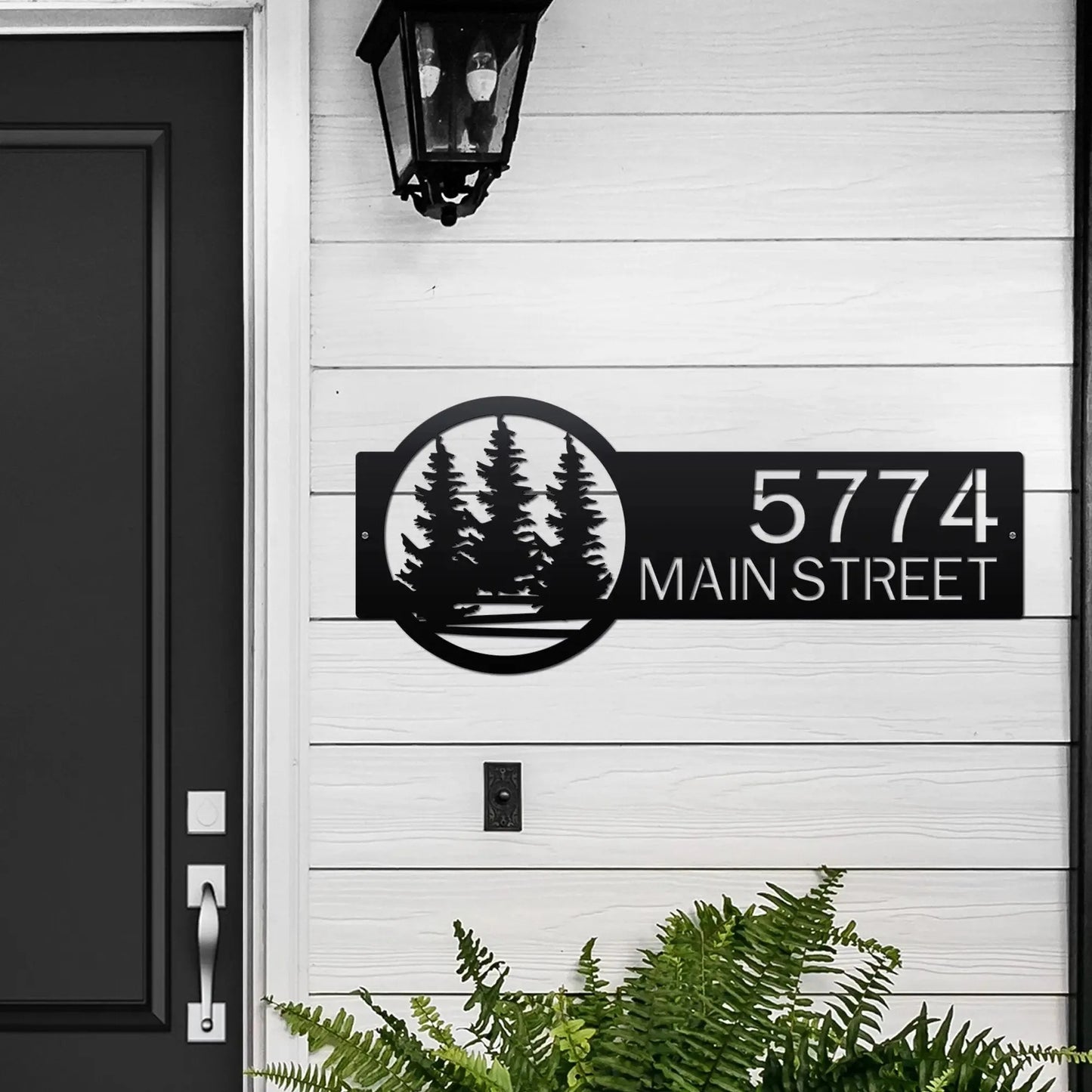 Evergreen Pine Trees Address Sign featuring custom house numbers and street name, crafted from high-quality steel with laser-cut precision, showcasing a black door backdrop and surrounding greenery.