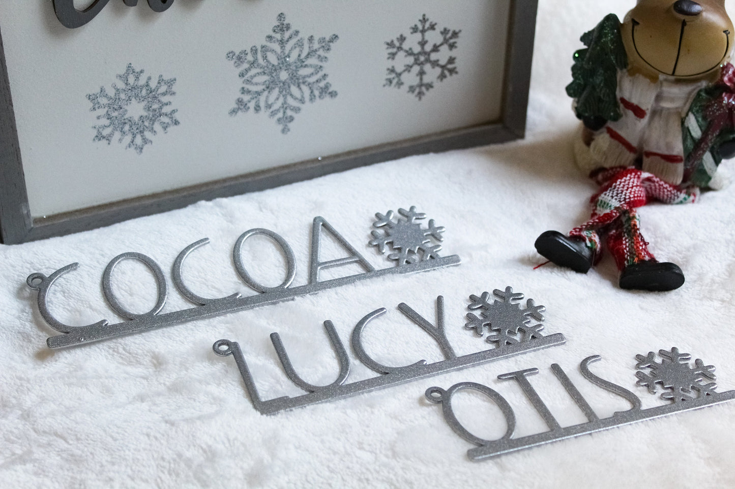 Christmas Stocking Name Tags Metal With Snowflake - Custom made; features laser-cut silver letters on a white surface, adorned with intricate snowflake designs, showcasing unique personalization for festive decor.