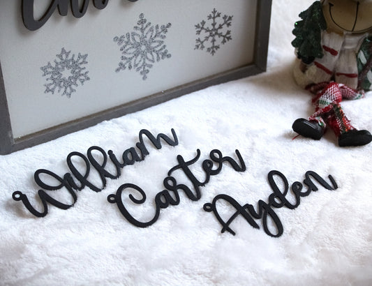 Metal Christmas Stocking Name Tags showcasing laser-cut black letters on a white surface, personalized and handcrafted from mild steel, ideal for festive decor like stockings, packages, or trees.