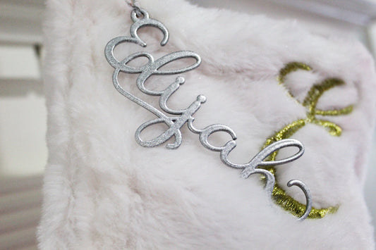 Christmas Metal Stocking Tags - Personalized Metal Tags Name for Christmas Stockings resting on a white fur surface, showcasing a sleek, laser-cut design typical of HouseSensationsArt's custom craftsmanship.