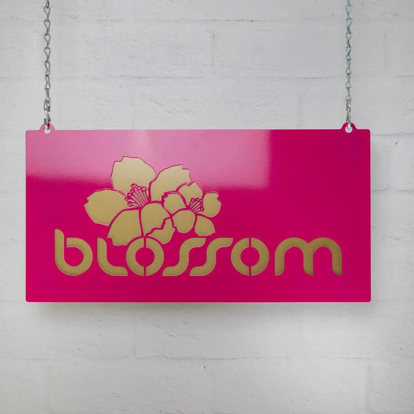 Single-Faced Hanging Custom Metal Business Sign displayed against a white brick wall, showcasing its dual-layer steel design with gold text and floral motifs, ideal for branding in storefronts or offices.