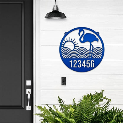 Flamingo Address Sign – Custom House Numbers Sign featuring a blue circle with a bird and numbers, set on a white wall, surrounded by green leaves. Perfect for home décor and gifting.