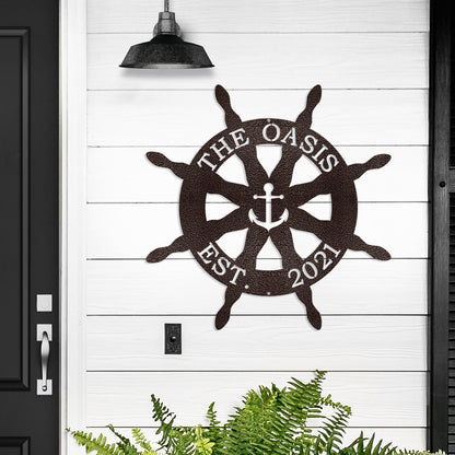 Nautical Captain's Ship Wheel Metal Door Hanger featuring a detailed metal wheel with an anchor design, ideal for personalized beach house decor or as a boater gift, mounted on a wall.