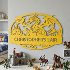 An oval dragon sign with large dragon silhouette, castle, & mountains that reads "CHRISTOPHER'S LAIR". Sign is finished in Spring Yellow and is shown displayed as bedroom wall art in dragon kids room above dragon figurines