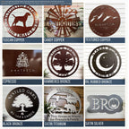 9-panel finish and color chart for custom metal signs featuring earthy and metallic tones. Top row includes Tuscan Copper dog-themed sign, Candy Copper personalized windmill sign, and Textured Copper mountain elevation sign. Middle row shows Espresso logo plaque, Hammered Bronze tree farm sign, and Oil Rubbed Bronze moon-and-stars camping sign. Bottom row features Black Bronze oak tree sign, Satin Titanium cabin and bear welcome sign, and Satin Silver monogram plaque.