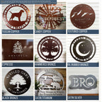 9-panel finish and color chart for custom metal signs featuring earthy and metallic tones. Top row includes Tuscan Copper dog-themed sign, Candy Copper personalized windmill sign, and Textured Copper mountain elevation sign. Middle row shows Espresso logo plaque, Hammered Bronze tree farm sign, and Oil Rubbed Bronze moon-and-stars camping sign. Bottom row features Black Bronze oak tree sign, Satin Titanium cabin and bear welcome sign, and Satin Silver monogram plaque.