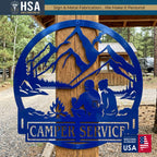 Blue circular metal camper name sign with a camping couple by a campfire, mountains and pines, reading CAMPER SERVICE for RV decor.