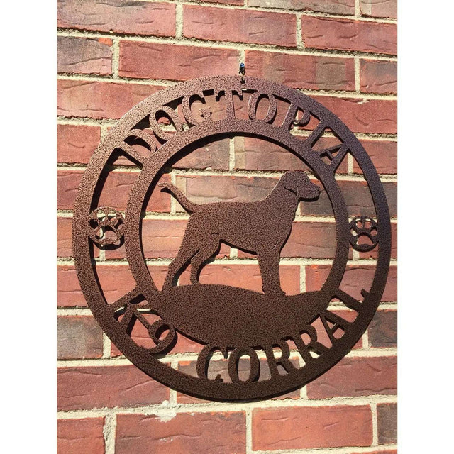 A textured copper metal wall sign showing a Labrador dog silhouette standing, with “DOGTOPIA,” “K-9 KORRAL,” and paw prints on each side.
