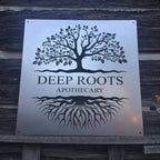 Large custom laser-cut metal business logo sign featuring a tree design and “Deep Roots Apothecary” text on a wooden background, ideal for storefront or office wall décor – House Sensations Art.