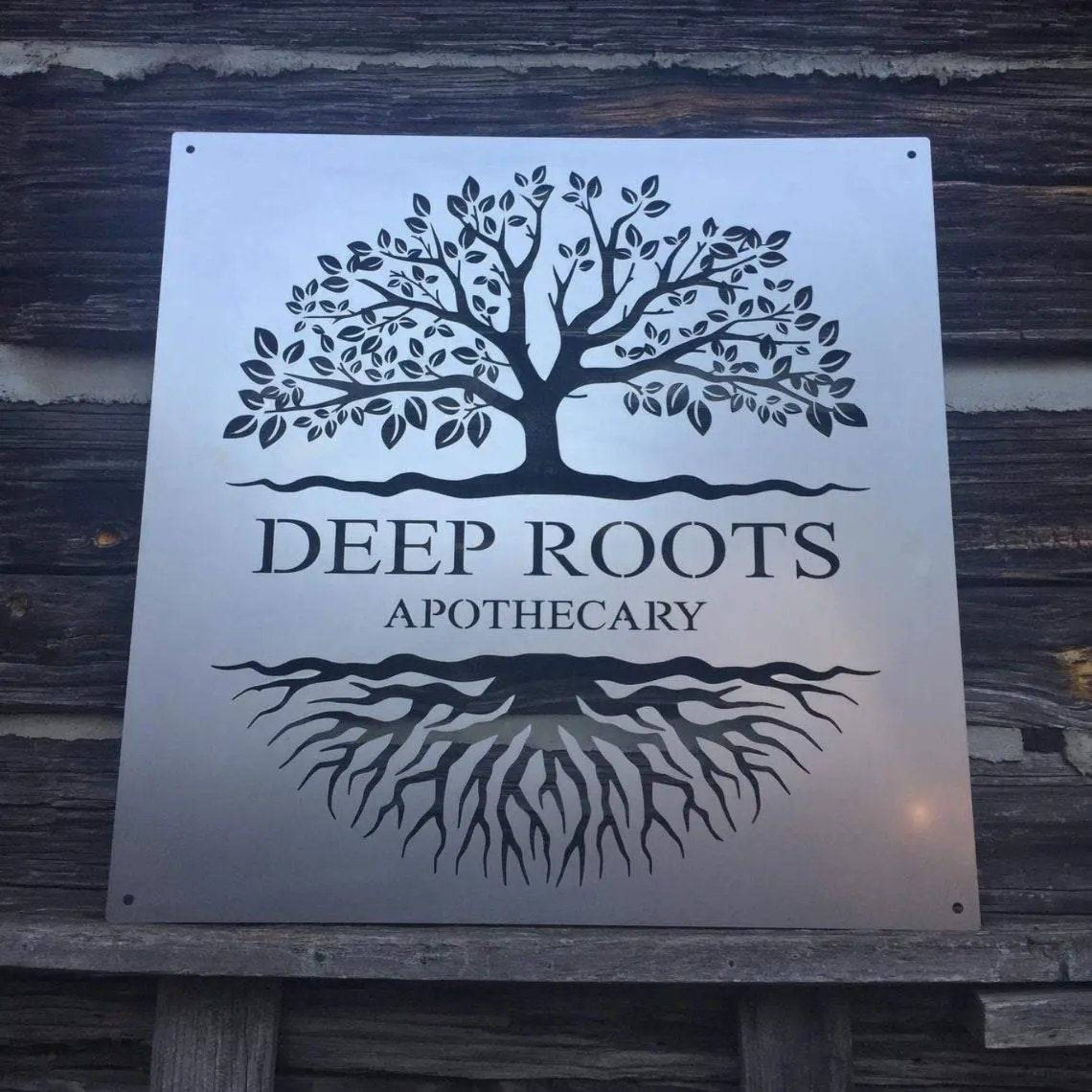 Large custom laser-cut metal business logo sign featuring a tree design and “Deep Roots Apothecary” text on a wooden background, ideal for storefront or office wall décor – House Sensations Art.