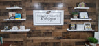Large custom laser-cut metal business logo sign for "Family Finances Redesigned" mounted on a wooden wall with shelves displaying decorative items – House Sensations Art.