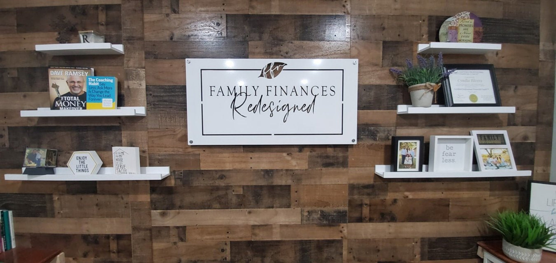 Large custom laser-cut metal business logo sign for "Family Finances Redesigned" mounted on a wooden wall with shelves displaying decorative items – House Sensations Art.