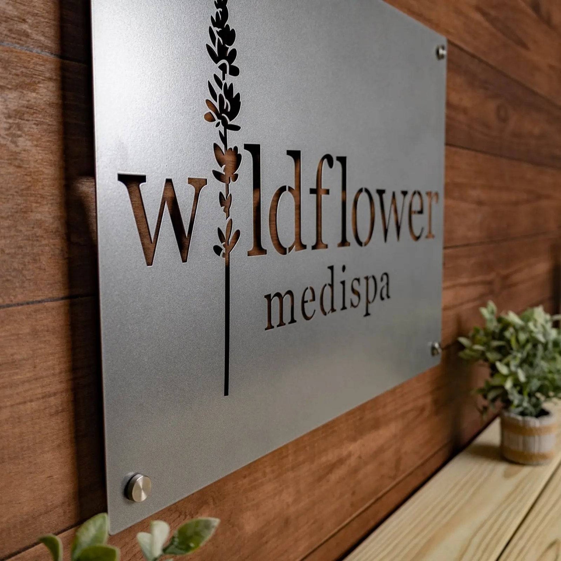 Large custom laser-cut metal business logo sign for “Wildflower Medispa” displayed on a wooden wall, perfect for office or storefront décor from House Sensations Art.