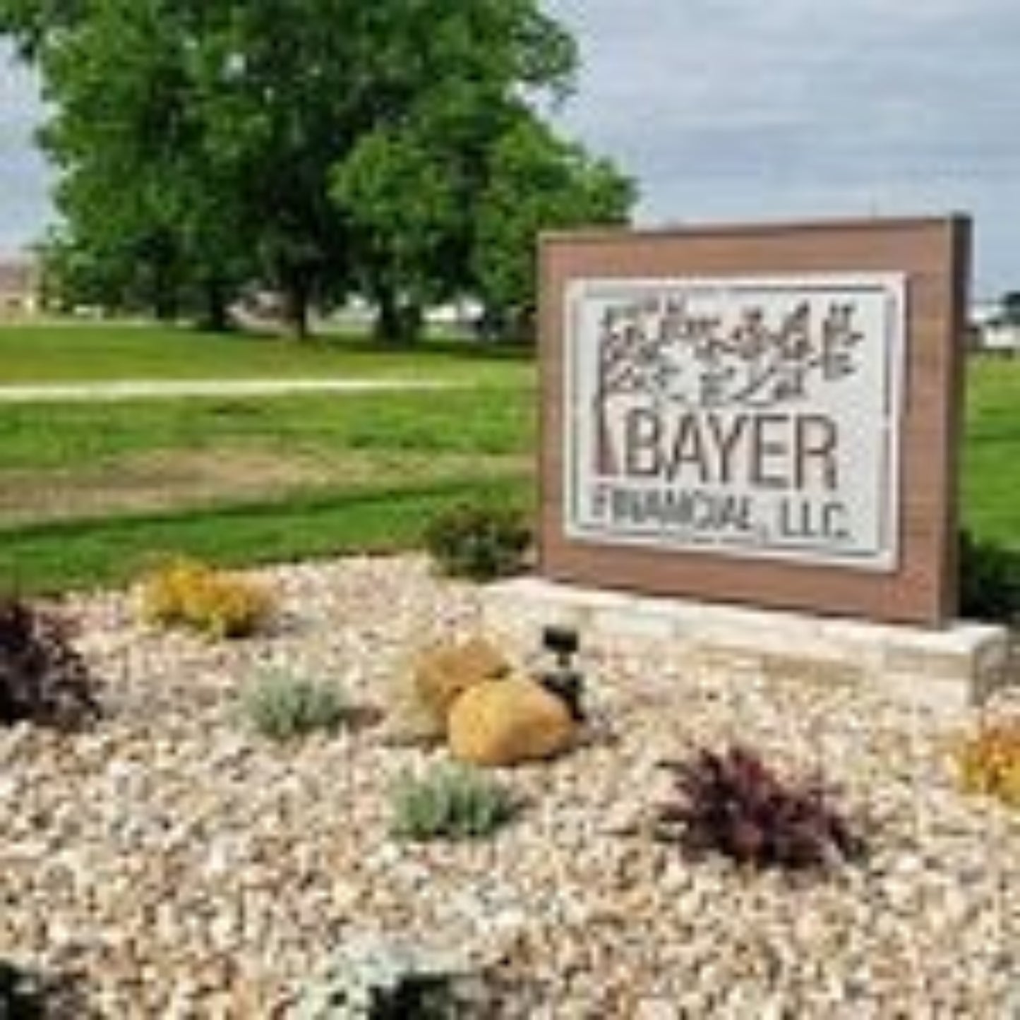 Large custom laser-cut metal business logo sign for "Bayer Financial LLC" displayed outdoors in a landscaped area with rocks and plants – House Sensations Art.