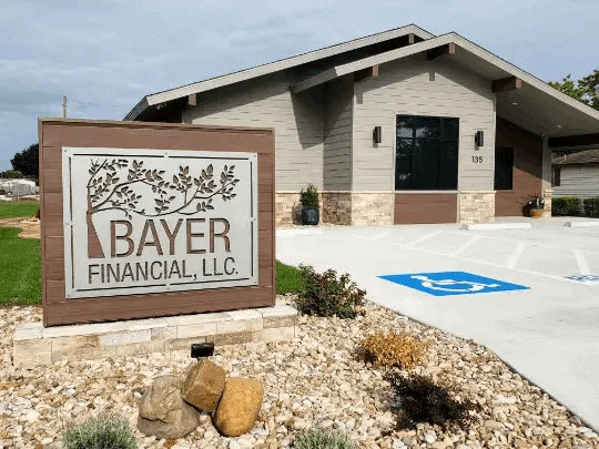 Custom metal sign for BAYER FINANCIAL, LLC with tree branch design, mounted on wood frame in landscaped outdoor setting.