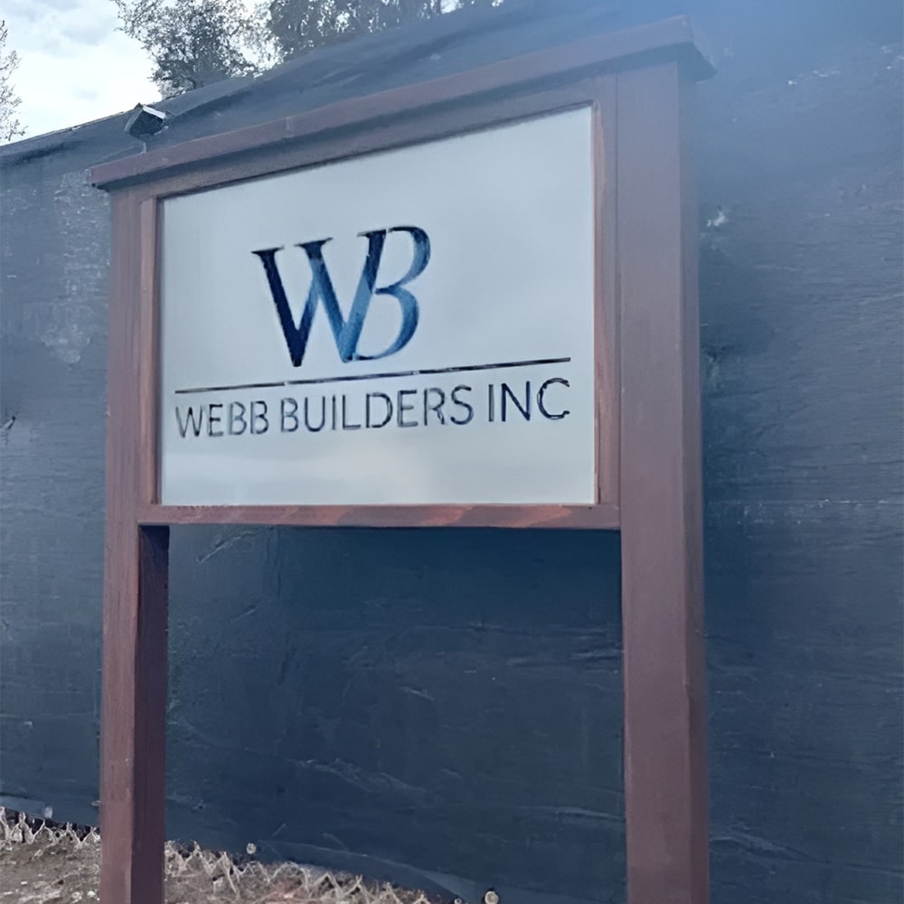 Custom metal office and storefront sign featuring laser-cut “Webb Builders Inc” logo, steel wall décor framed in wood on dark backdrop.