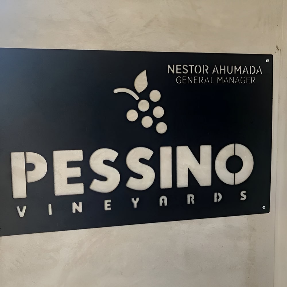 Custom metal office and storefront plaque with laser-cut “PESSINO VINEYARDS” logo and “Nestor Ahumada General Manager” text, decorative steel signage on black background.
