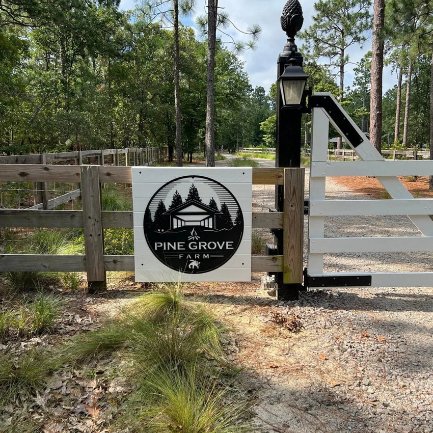 Custom metal office and storefront sign featuring laser-cut “Pine Grove Farm” logo mounted on a white gate, decorative steel signage in a forested setting.