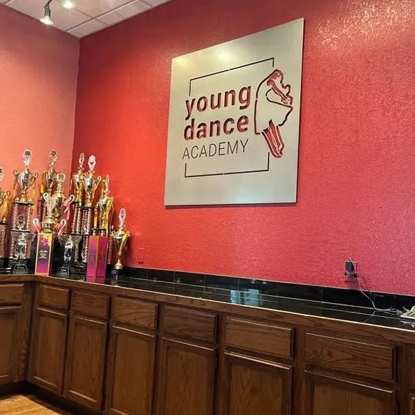Custom metal office and storefront sign featuring laser-cut “Young Dance Academy” logo, steel wall décor on red background with trophies on counter.