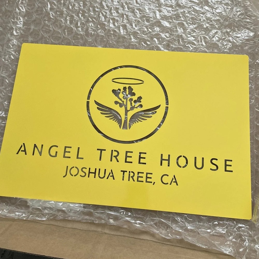 Custom metal office and storefront sign with laser-cut “Angel Tree House Joshua Tree, CA” logo, yellow steel wall décor on textured background.