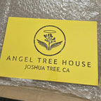 Custom metal office and storefront sign with laser-cut “Angel Tree House Joshua Tree, CA” logo, yellow steel wall décor on textured background.