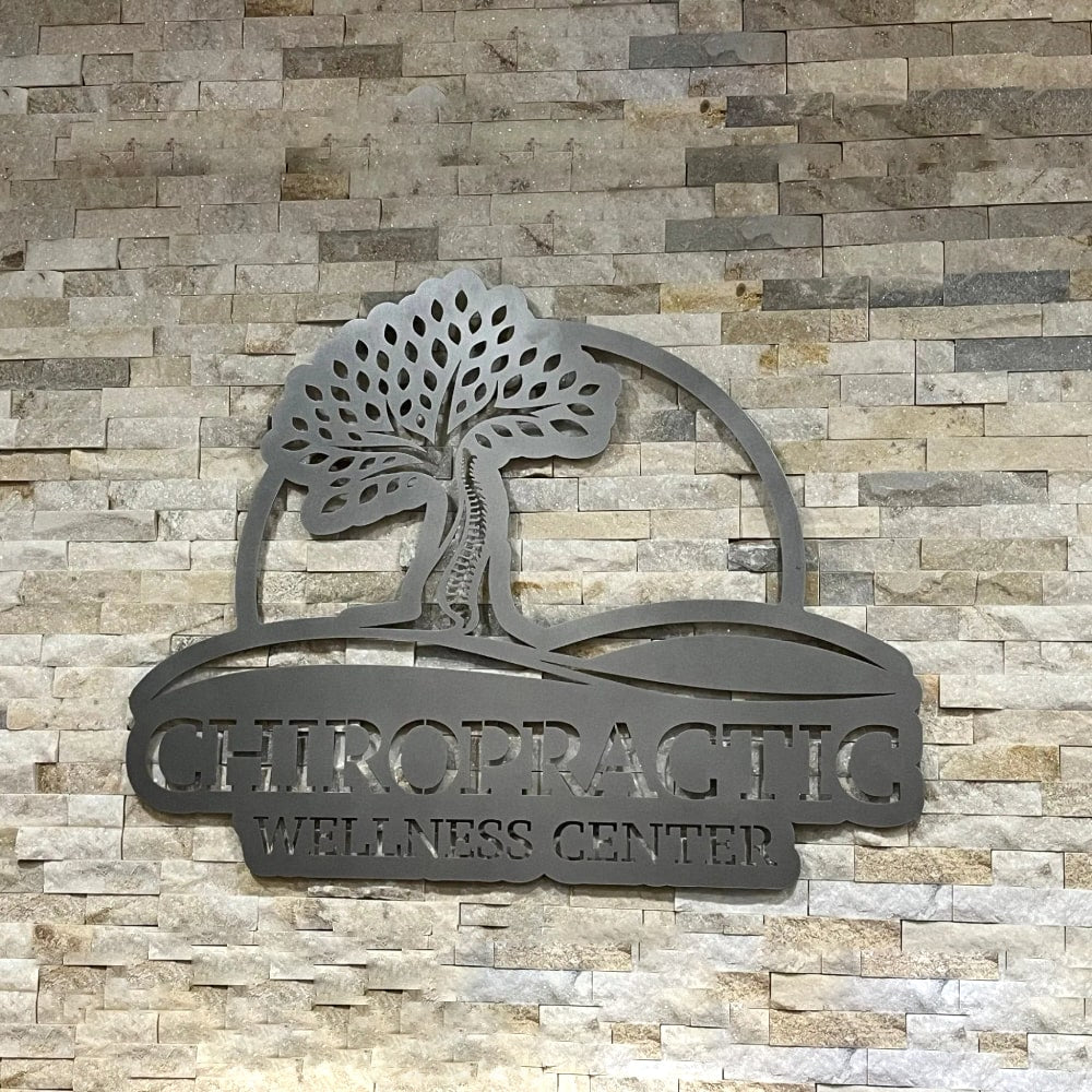 Custom metal office and storefront sign featuring laser-cut “Chiropractic Wellness Center” logo, steel wall décor on textured stone wall.