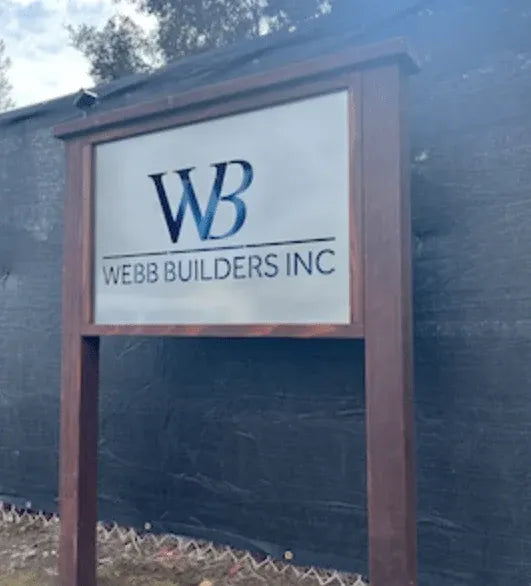 White rectangular sign in wood frame displays bold “WEBB BUILDERS INC” and stylized “WB” logo.