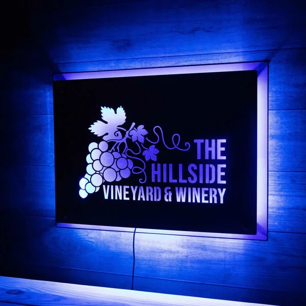Illuminated metal sign for “The Hillside Vineyard & Winery” mounted on a wooden wall, featuring backlit lettering and decorative design for a vibrant, eye-catching display.