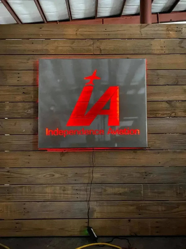 Red backlit 3D sign on wood wall: “Independence Aviation” with “IA” airplane logo and glowing edges.
