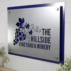 Metal sign featuring “The Hillside Vineyard & Winery” logo mounted on a white wall, showcasing elegant branding and durable craftsmanship.