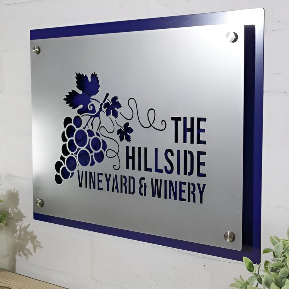 Metal sign featuring “The Hillside Vineyard & Winery” logo mounted on a white wall, showcasing elegant branding and durable craftsmanship.