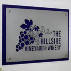 Metal sign featuring “The Hillside Vineyard & Winery” logo displayed on a white background, showcasing crisp, professional branding and durable metal construction.