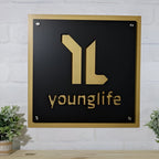 Black metal plaque featuring a gold “younglife” logo mounted on a white brick wall, showcasing a sleek and elegant branded design.