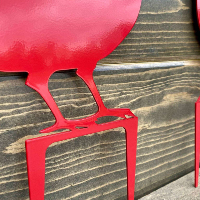 Close-up of red metal bird sign showing laser-cut feet and pointed stakes, highlighting texture and precision craftsmanship.