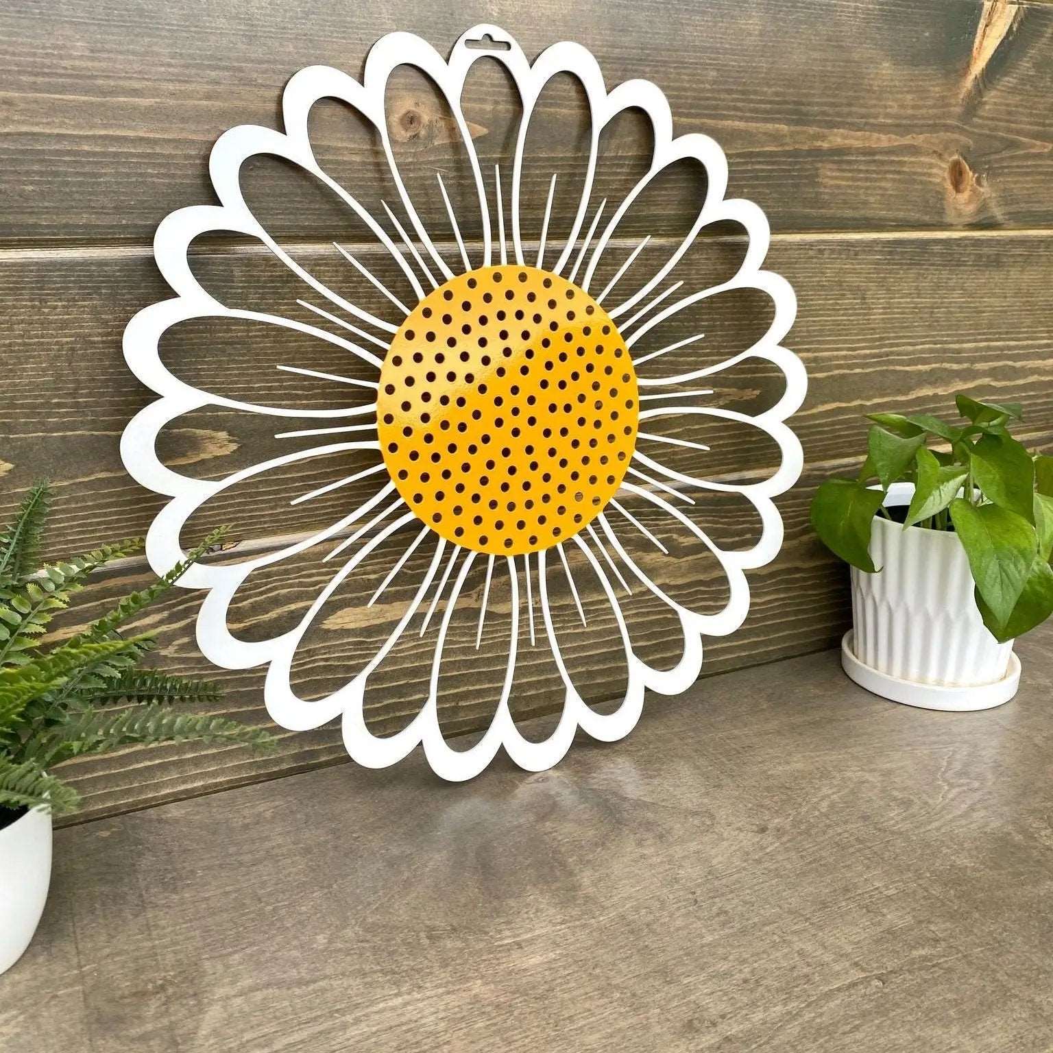 Decorative metal wall art of sunflower with yellow center and white petals on wooden surface, custom indoor or outdoor home décor accent