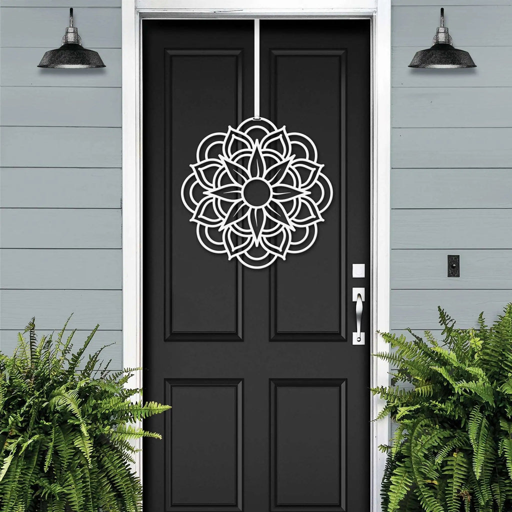 Handcrafted metal flower wreath on black front door, white decorative pattern, gray exterior wall, modern outdoor metal door decor, elegant home entry art