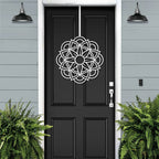 Handcrafted metal flower wreath on black front door, white decorative pattern, gray exterior wall, modern outdoor metal door decor, elegant home entry art