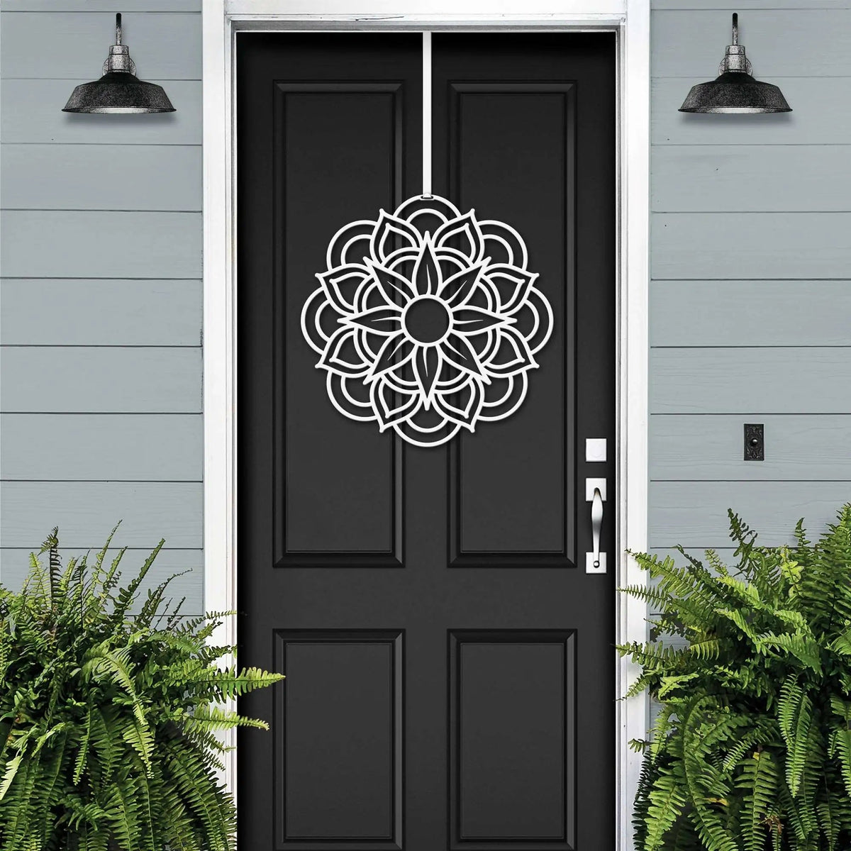 Handcrafted metal flower wreath on black front door, white decorative pattern, gray exterior wall, modern outdoor metal door decor, elegant home entry art