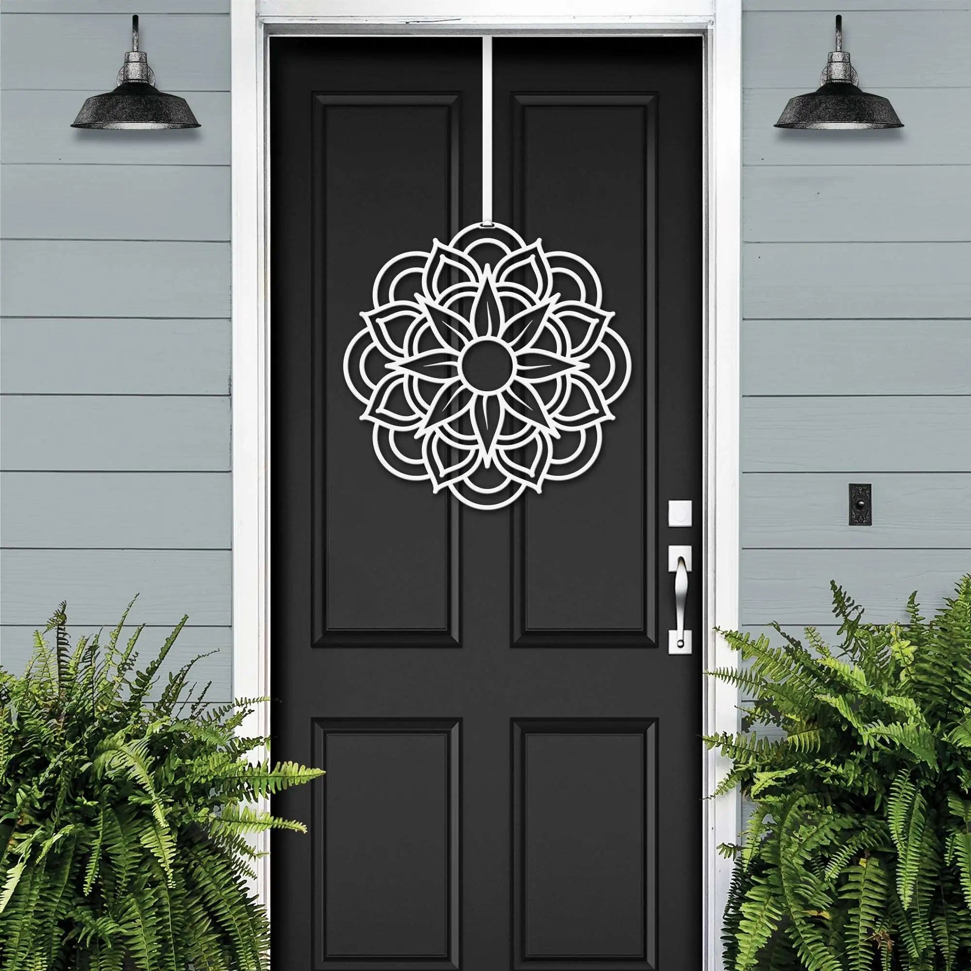 Handcrafted metal flower wreath on black front door, white decorative pattern, gray exterior wall, modern outdoor metal door decor, elegant home entry art