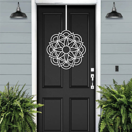 Handcrafted metal flower wreath on black front door, white decorative pattern, gray exterior wall, modern outdoor metal door decor, elegant home entry art